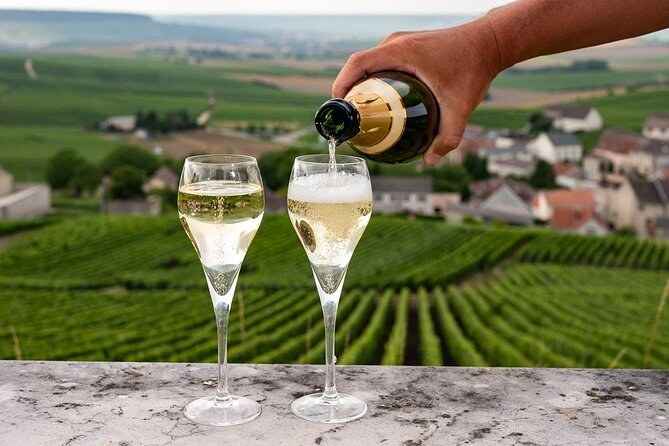 Champagne poured into two flutes above a slope of vines