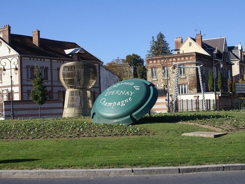 A giant champagne capsule naming Épernay on a roundabout, a giant cork beside it
